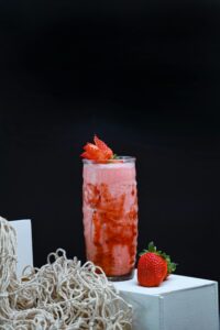 A delicious and healthy strawberry smoothie in a glass on a white stand with a dark background.