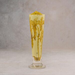 Refreshing mango lassi in a tall glass with crunchy toppings on a gray background.