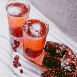 pomegranate juice with ice cubes and fresh fruit on a table.