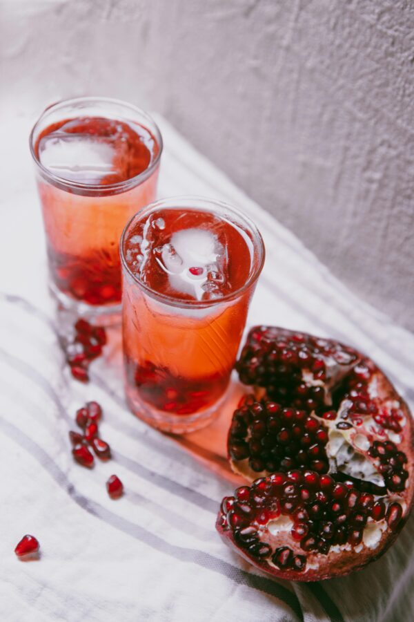 pomegranate juice with ice cubes and fresh fruit on a table.